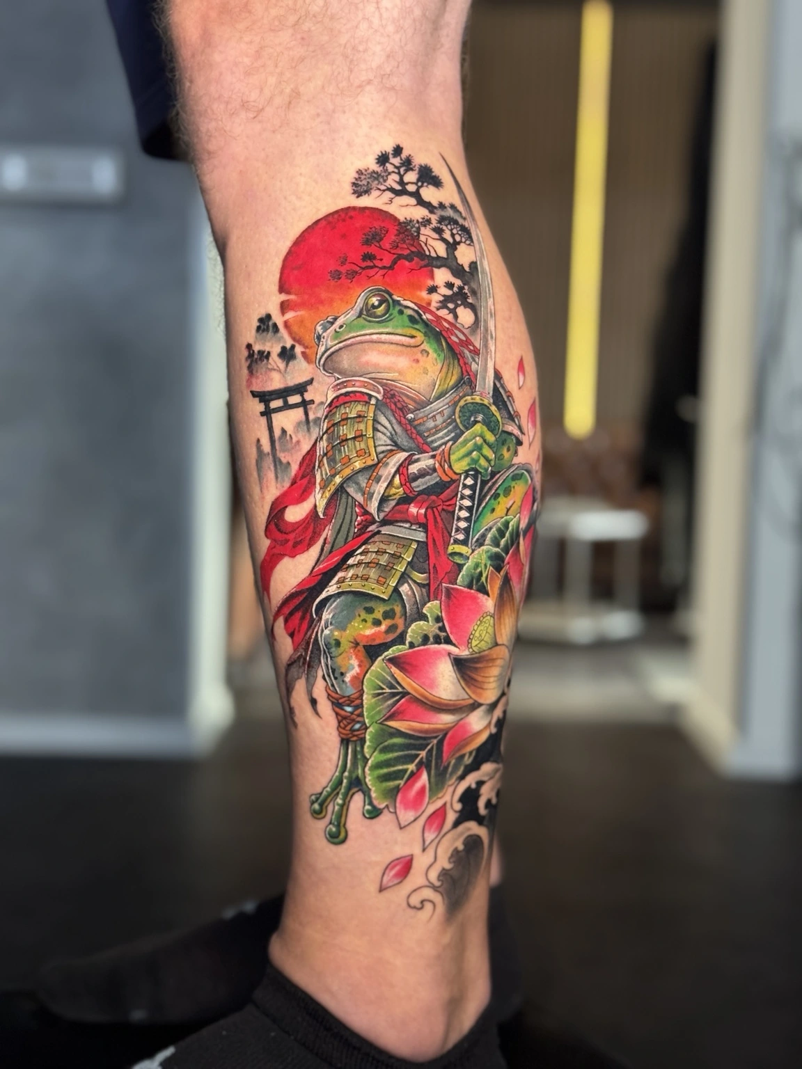 Farbiges Samurai-Frosch-Tattoo am Unterschenkel mit roter Sonne und Blüten